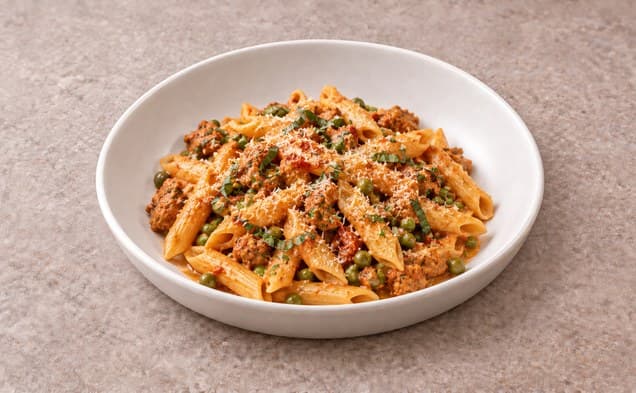 A serving of spicy chicken pasta and peas with sun-dried tomato sauce on a plain white dish