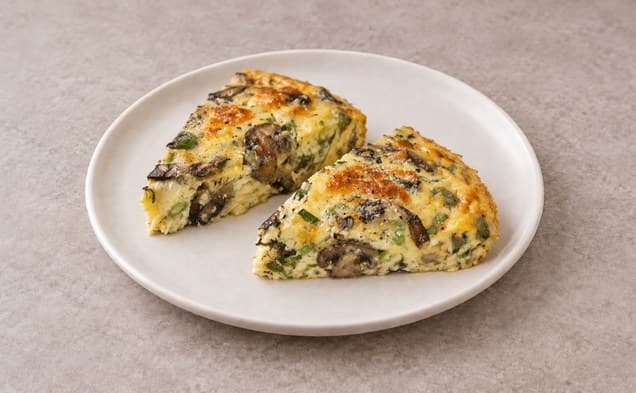 A serving of frittata with mushrooms, thyme, and parmigiano cheese on a plain white dish