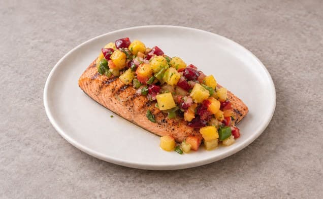 A serving of grilled salmon with cherry, pineapple, mango salsa on a plain white dish